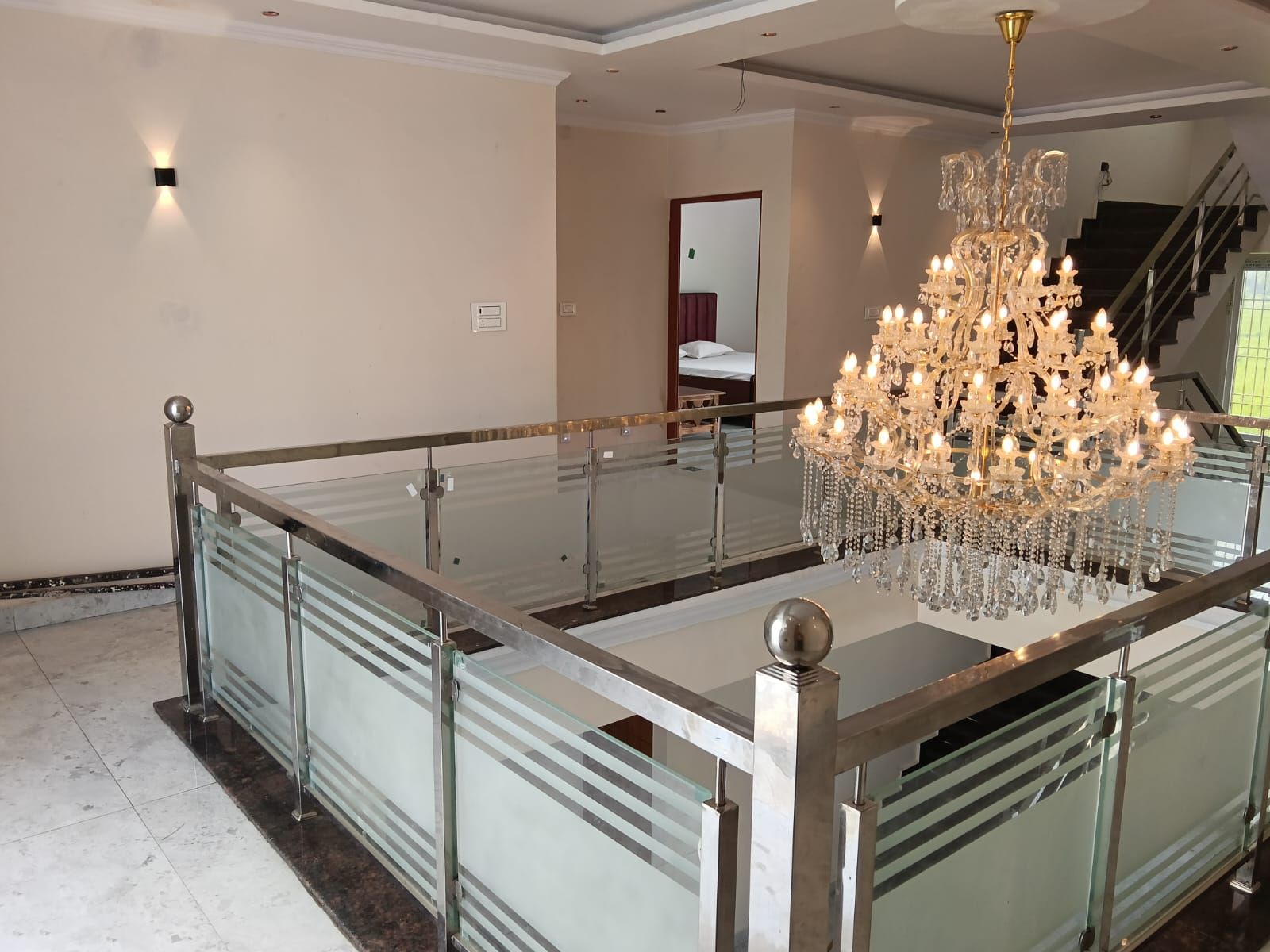 Un vestíbulo de hotel espacioso con una gran araña de cristal, una barandilla de vidrio y una escalera que conduce a un piso superior.
