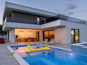 Ein modernes, zweistöckiges Haus mit Swimmingpool, Essbereich im Freien und überdachter Terrasse.