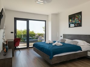 Ein modernes Schlafzimmer mit einem großen Bett, einem roten Sessel, einem Gemälde und Blick durch eine Schiebetür.