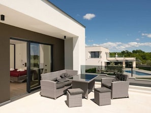 Ein moderner Außenbereich mit Glasdoor, das zu einem Schlafzimmer führt, sowie ein Pool und ein Haus im Hintergrund.