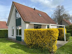 A residential house with a sloped roof, a visible chimney, and a well-maintained hedge in the foreground. - Beautiful Holiday Home on the Beach (Breskens)