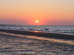 A beach with a sunset, waves, and a pier. - Beautiful Holiday Home on the Beach (Breskens)