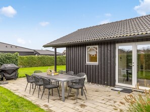 A patio with a table and chairs, a barbecue grill, and a wooden building with a tiled roof. - "Ellanor" - 100m from the sea by Interhome (Broager)