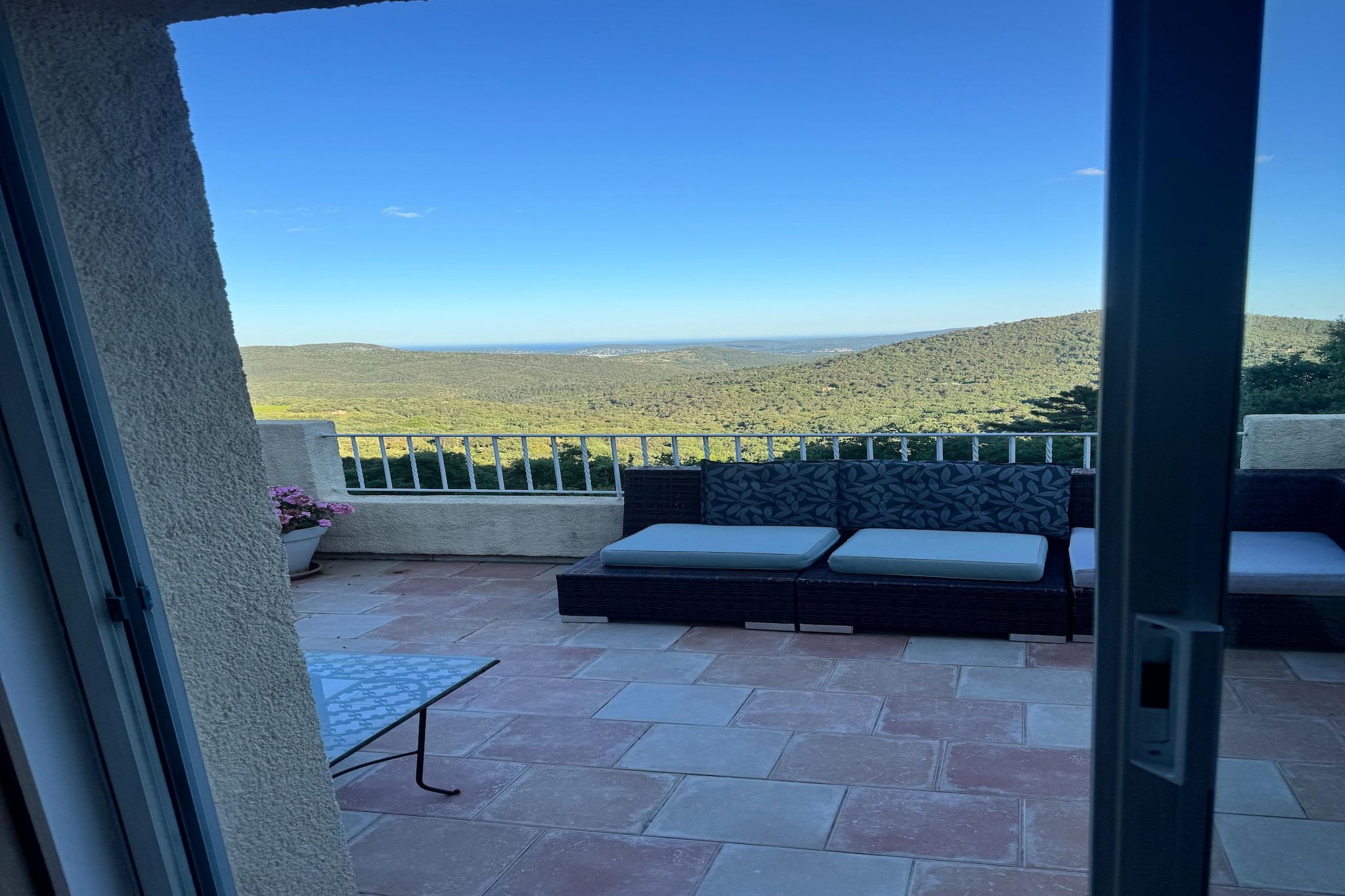 A balcony with a sofa and a table, overlooking a hilly landscape.