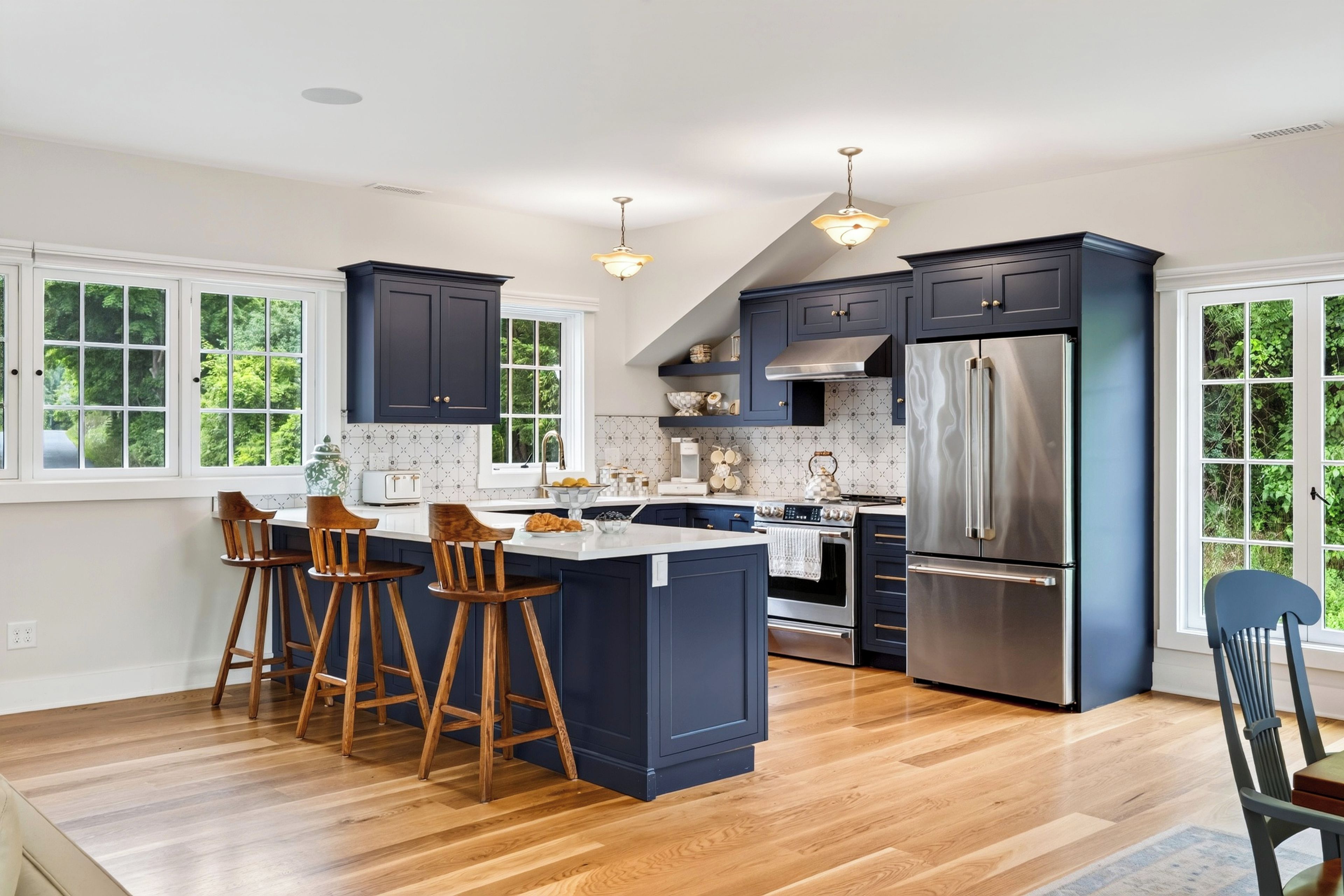 A kitchen with a central island, dark cabinetry, stainless steel appliances, and a view of greenery through large windows.