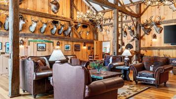 A rustic interior with wooden walls, mounted animal heads, leather furniture, and a chandelier.