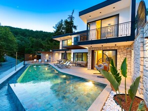 Ein modernes, zweistöckiges Haus mit Swimmingpool, Außenbereich zum Sitzen und einer Steinfassade.