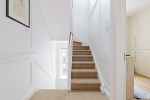 A staircase with a carpeted landing leading to a room with white walls and a door. - Classically Elegant 3BDR Soho Townhouse (London)