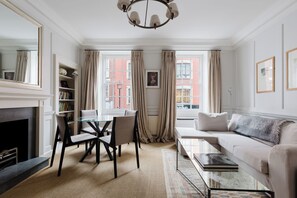 A well-lit living room with a fireplace, a dining area with a glass table, and a sofa with a throw blanket. - Classically Elegant 3BDR Soho Townhouse (London)