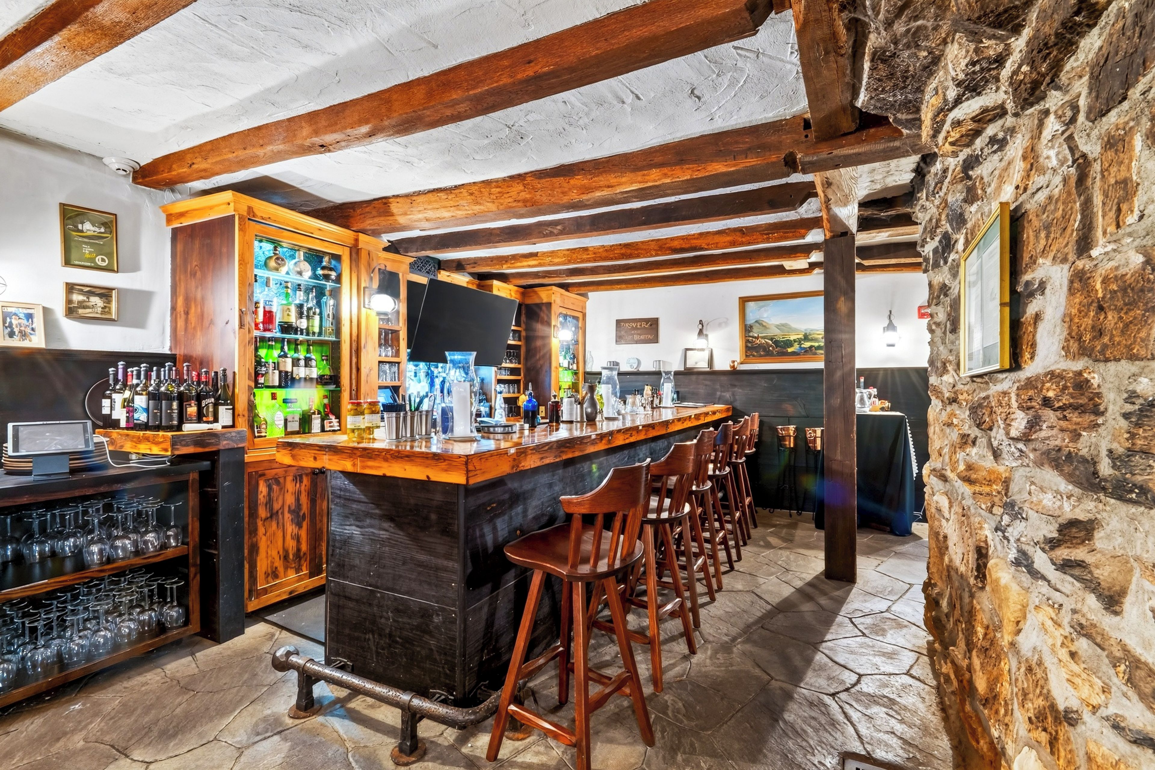 Eine Bar mit Holzbalken, einer Steinwand und einer Theke mit Hockstühlen.