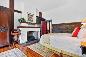 Une chambre à coucher avec une tête de lit en bois, un lit recouvert d’une couette blanche, une porte rouge, une cheminée et un plancher en bois.