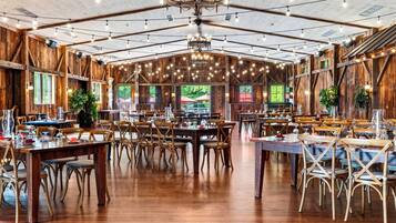 A spacious indoor dining area with wooden walls and ceilings, multiple tables set for dining, and a large chandelier.