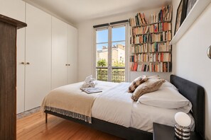 Ein Schlafzimmer mit einem Bett, einem Nachttisch, einem Bücherregal und einem Fenster.