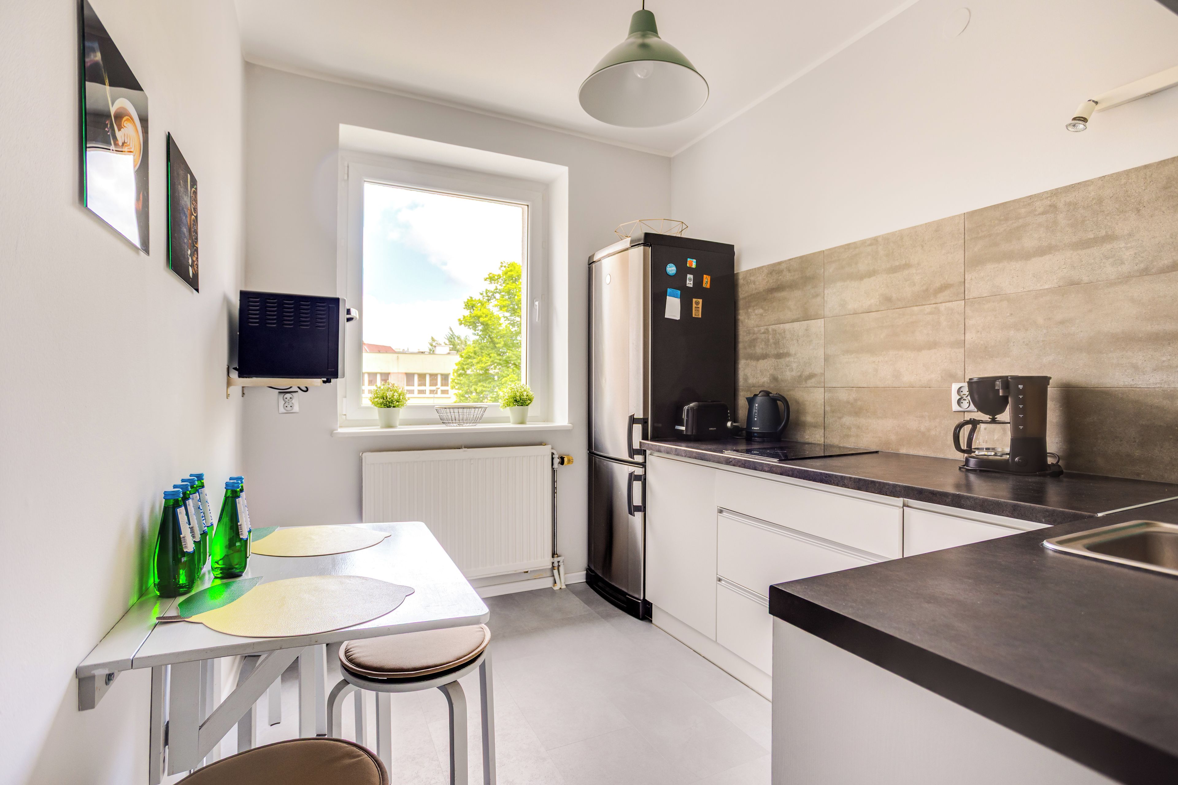 Una cocina moderna con refrigerador empotrado, ventana con vista a follaje y comedor con mesa y sillas.