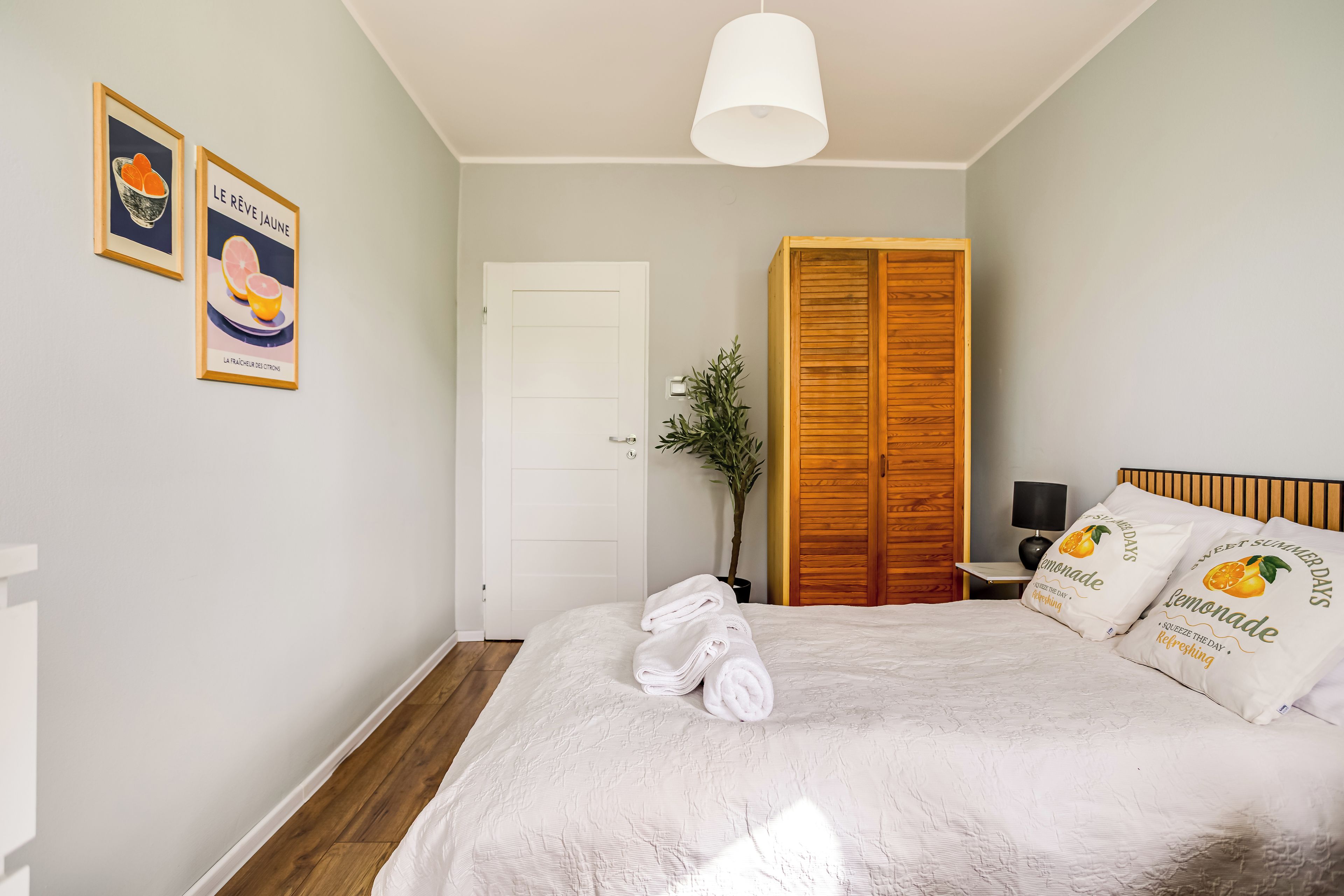 Un dormitorio con cama, armario, puerta y dos cuadros en la pared.