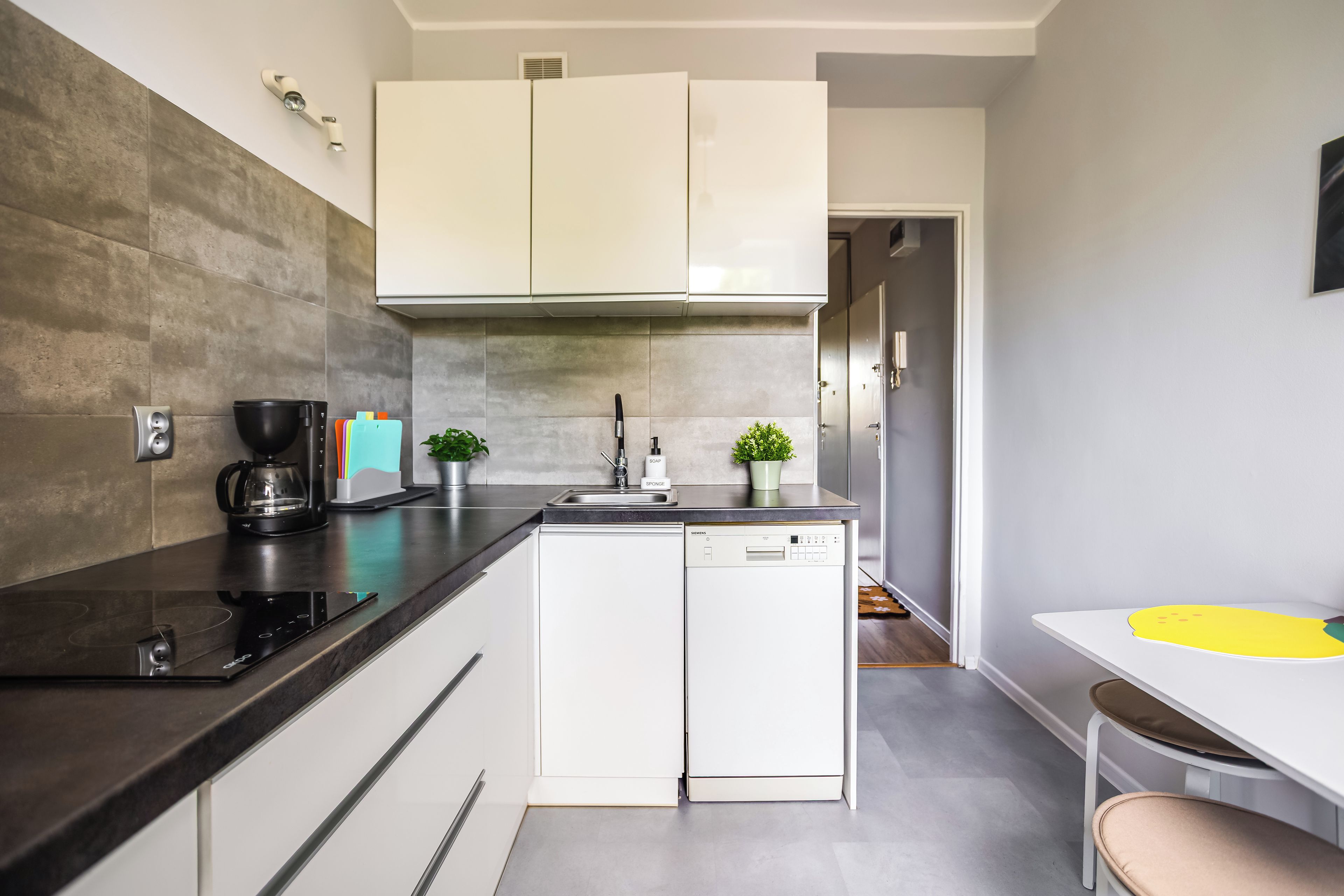 Una cocina moderna con lavavajillas integrado, cafetera y una pequeña planta en la encimera.