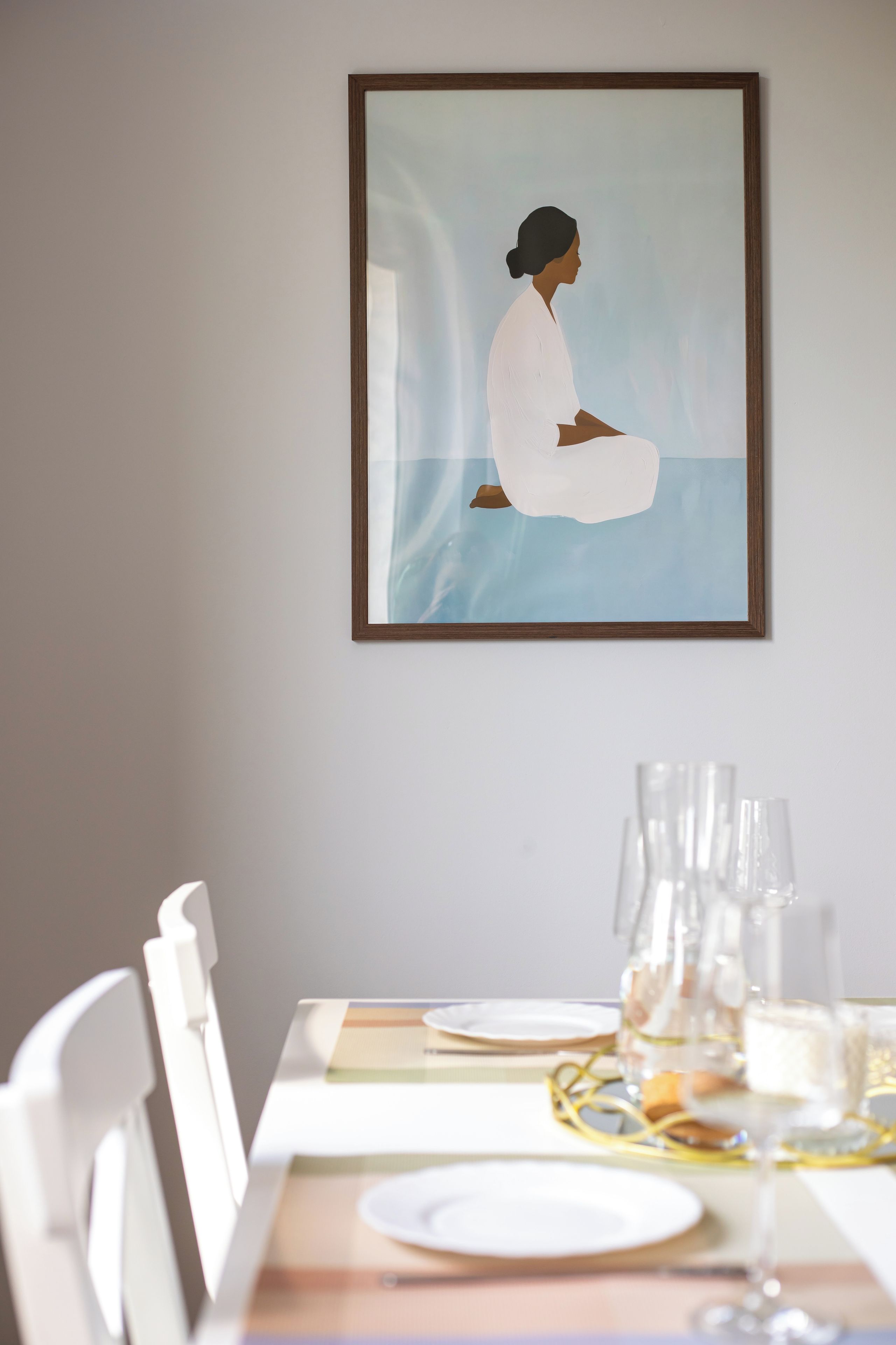 Un comedor con una mesa preparada para dos personas, una obra de arte enmarcada en la pared y una ventana que proporciona luz natural.