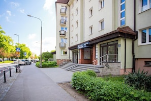 A multi-story building with a ground-level entrance, a staircase leading to the entrance, and a sidewalk with a pedestrian crossing. - Jasny Apartament blisko Starego Browaru (Poznań)