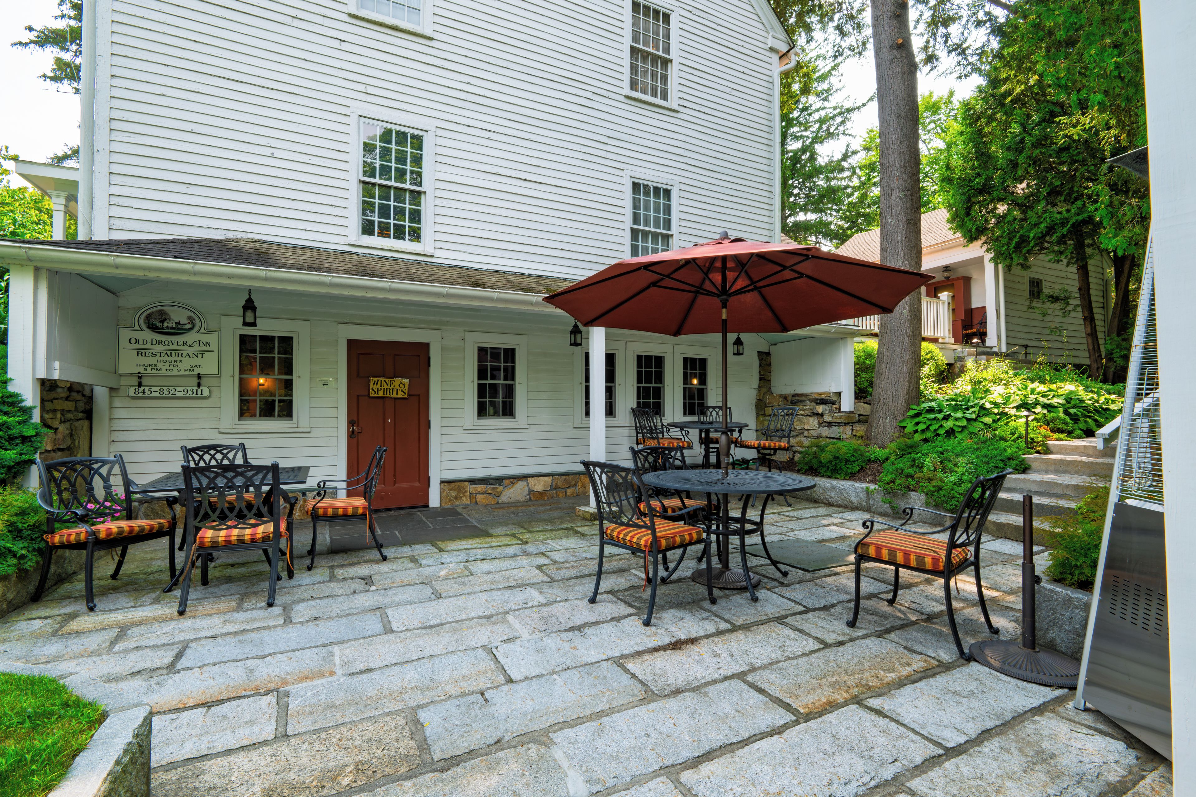 A patio area with stone flooring, outdoor seating with metal tables and chairs, and a red umbrella.