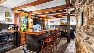 Un espace bar agrémenté de poutres en bois, d’un mur en pierre et d’un comptoir avec des tabourets.