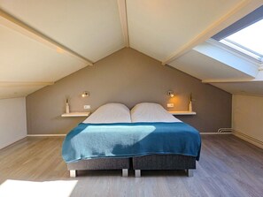 A bedroom with a sloped ceiling, a bed with a blue blanket, two bedside tables with lamps, and a skylight. - Uniquely Located Holiday Home Se12 (Serooskerke)