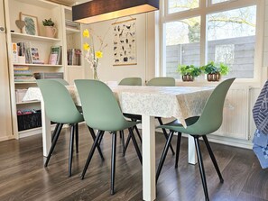 A dining area with a table set for four, surrounded by green chairs, a bookshelf, and a wall-mounted dog illustration. - Uniquely Located Holiday Home Se12 (Serooskerke)