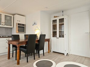Ein Essbereich mit Holztisch und -stühlen, eine Küche mit weißen Schränken und ein weißer Schrank mit Glastüren.