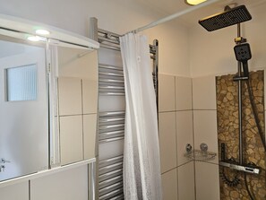Eine Dusche mit Handbrause, einer Duschwanne aus Glas und einem Duschvorhang.