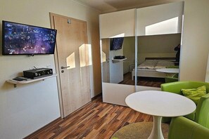 A compact room with a bed, a television mounted on the wall, a small table, and a green chair. - Holiday home with 2 bedrooms (Ostseebad Prerow)