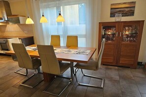 A dining area with a wooden table, four chairs, and pendant lights. - Holiday home with 2 bedrooms (Ostseebad Prerow)