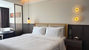 Et hotelværelse med seng, sengebord, lampe og vægmonteret lys.