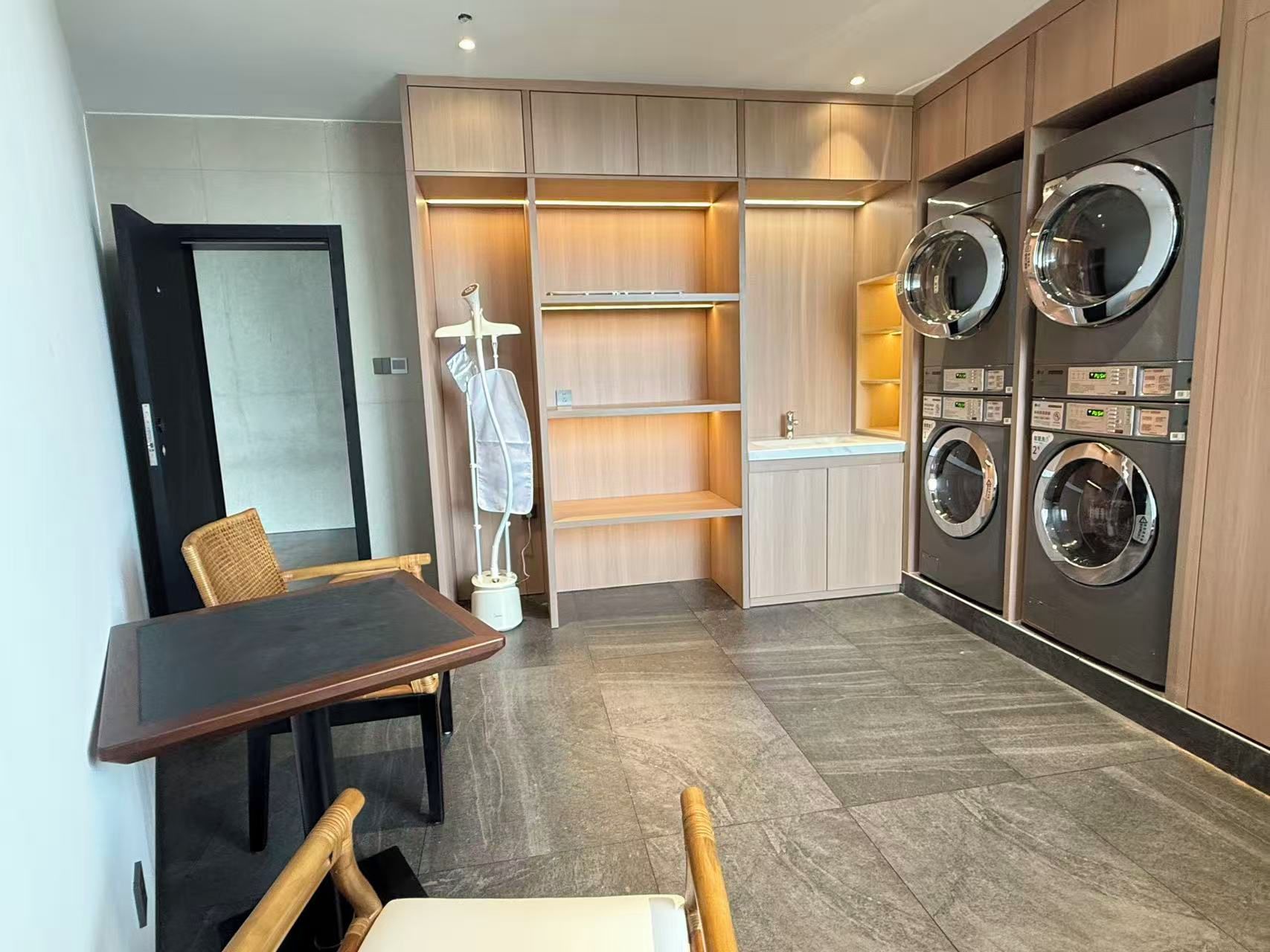 A compact laundry room with built-in washers and dryers, a small table with chairs, and a drying rack.