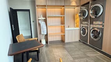 A compact laundry room with built-in washers and dryers, a small table with chairs, and a drying rack.