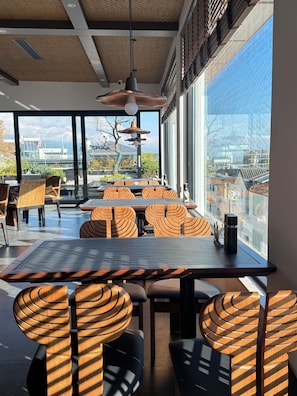 A modern dining area with a large table and chairs, large windows with a view of buildings and trees, and a ceiling with a woven pattern. - Wanda Moments Resort Dali Ancient City (Dali)