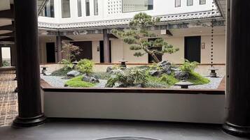 Un jardin intérieur paisible, agrémenté d’un élément aquatique, présentant une architecture de style japonais traditionnel et offrant une vue sur un bâtiment aux grandes fenêtres.