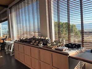 A kitchen with a long counter, wooden cabinets, and a view through large windows with blinds.