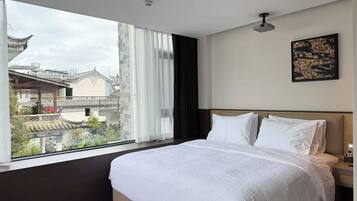 A hotel room with a large bed, a view of traditional architecture outside, and a ceiling fan.