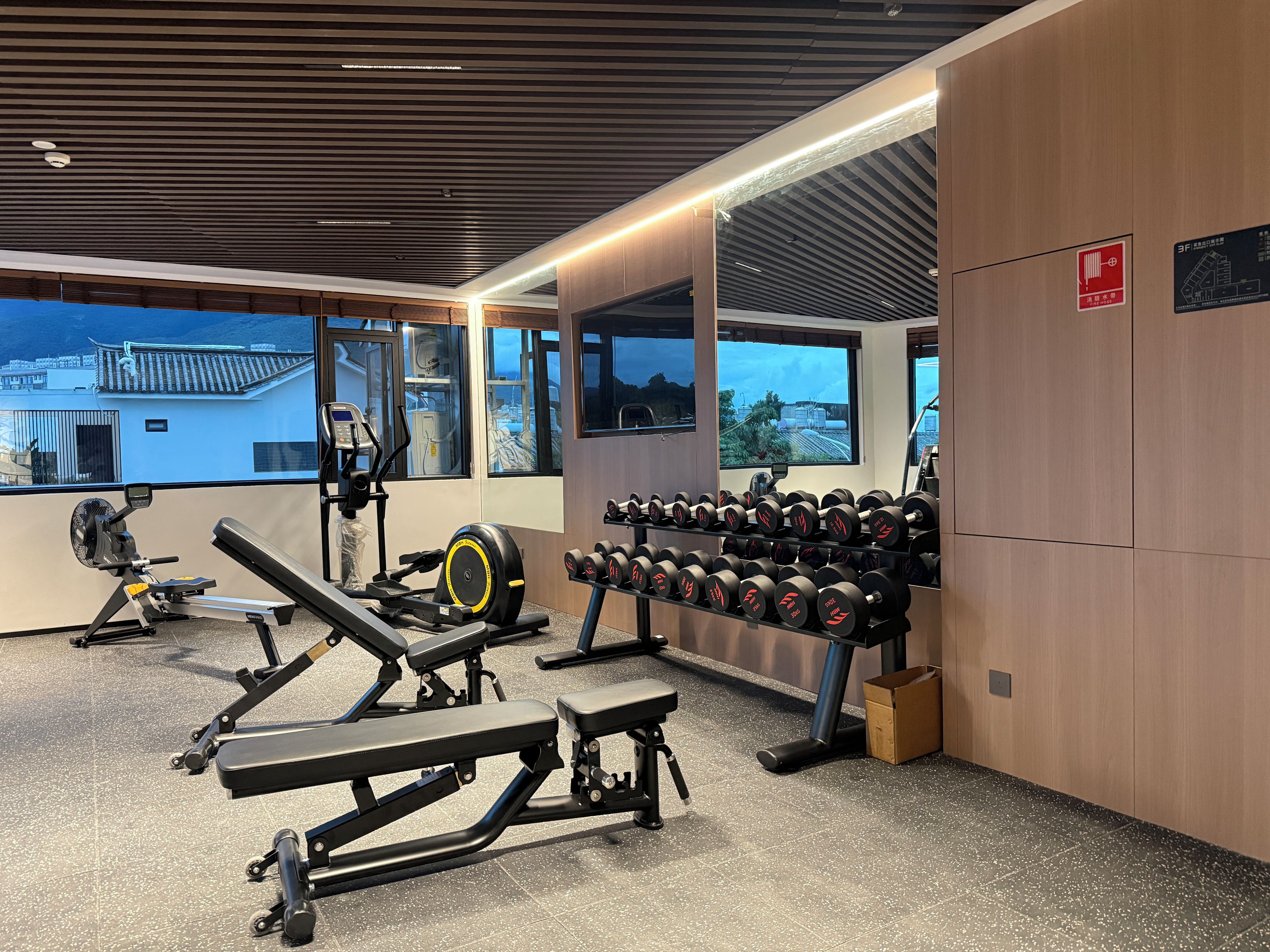 Une salle de sport équipée de matériel d’exercice, d’un porte-haltères et de grandes fenêtres offrant une vue dégagée.