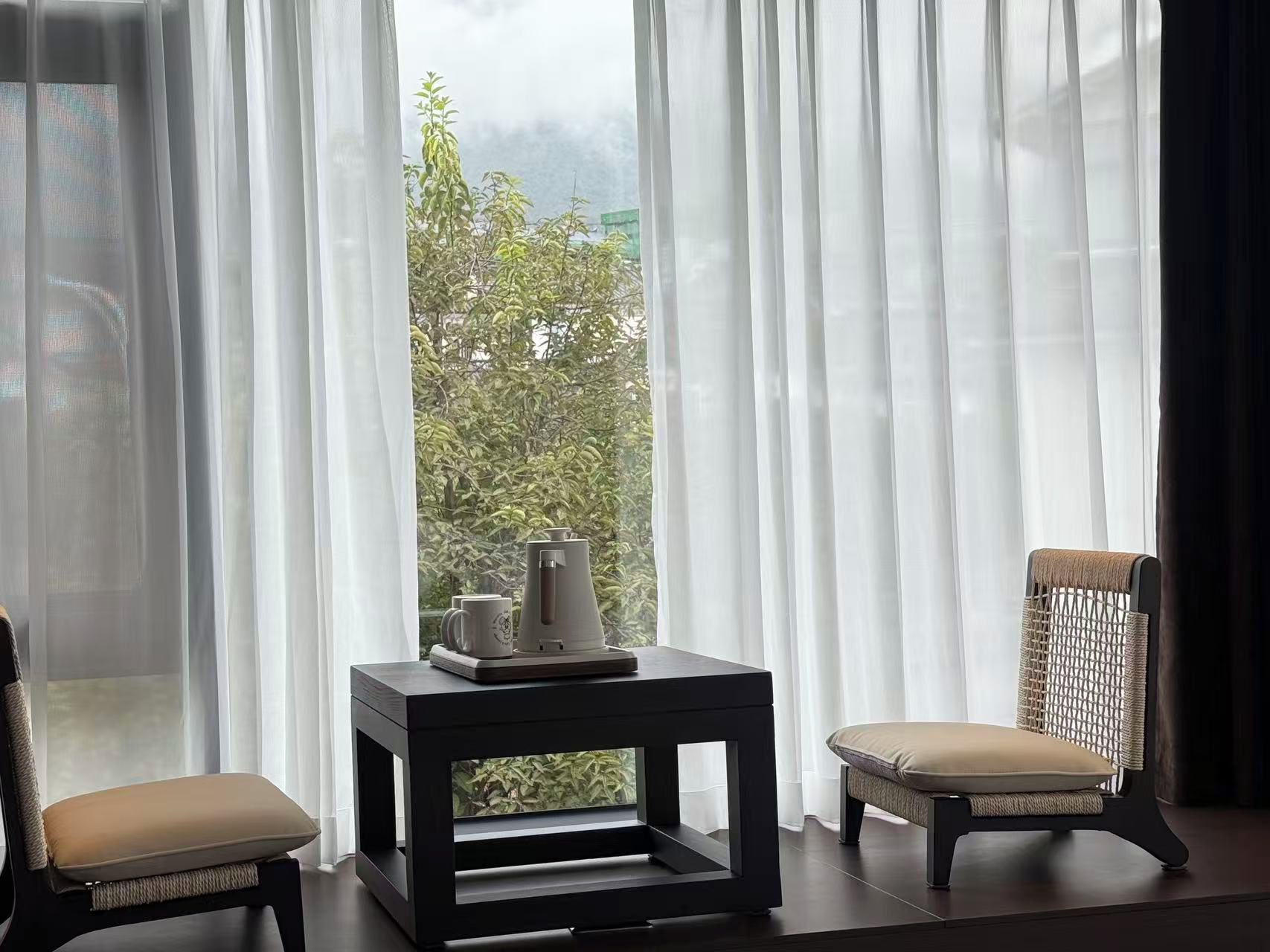 Una habitación con vistas, cortinas translúcidas, una mesita con bandeja y dos sillas.