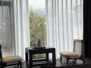 A room with a view through sheer curtains, a small table with a tray, and two chairs.