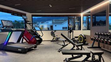 Un gimnasio con equipamiento cardiovascular, zonas de levantamiento de pesas y vistas a edificios a través de amplias ventanas.
