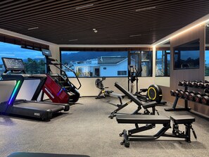 A gym with cardio equipment, weightlifting stations, and a view of buildings through large windows.