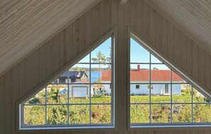 Una habitación con techo inclinado y dos grandes ventanales que ofrecen vistas a un edificio de tejados rojos y una zona con césped.