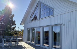 Una casa moderna con una amplia terraza, puertas correderas de vidrio y techo inclinado.
