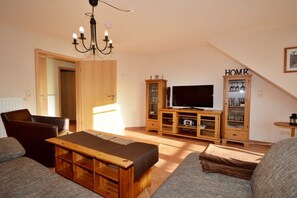 A living room with a sofa, a wooden bench, a television, and a cabinet with glass doors. - Holiday apartment with 2 bedrooms (Norddeich)
