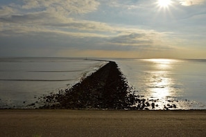 A beach with a long, narrow jetty extending into calm waters, under a partly cloudy sky with the sun low on the horizon. - Holiday apartment with 2 bedrooms (Norddeich)