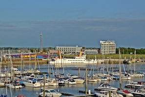 Un port esportiu amb nombroses embarcacions amarrades, un gran vaixell de creuer i un edifici de disseny modern al fons.