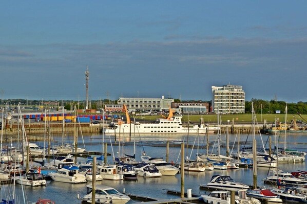 A marina with multiple boats docked, a large cruise ship, and a building with a modern design in the background. - Holiday apartment with 2 bedrooms (Norddeich)