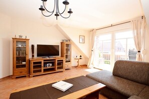 A living room with a television, wooden entertainment unit, and a sofa. - Holiday apartment with 2 bedrooms (Norddeich)