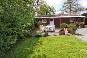 A red building with a tiled roof, a white door, and a window. There is a white table and chairs set outside. - Holiday home in Minsen with swimming pool (Minsen)